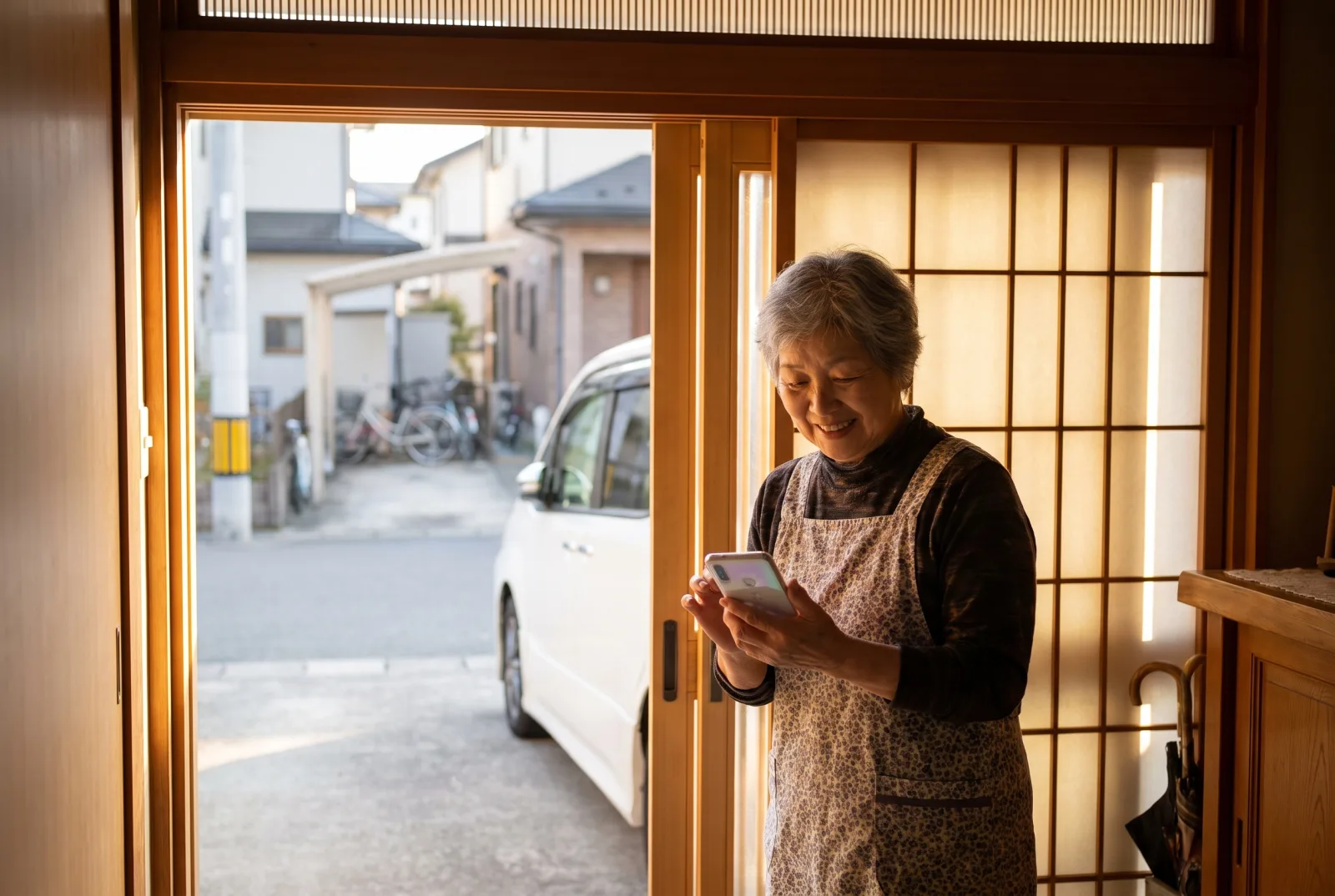 玄関でスマートフォンを見て微笑む家族。外には送迎車